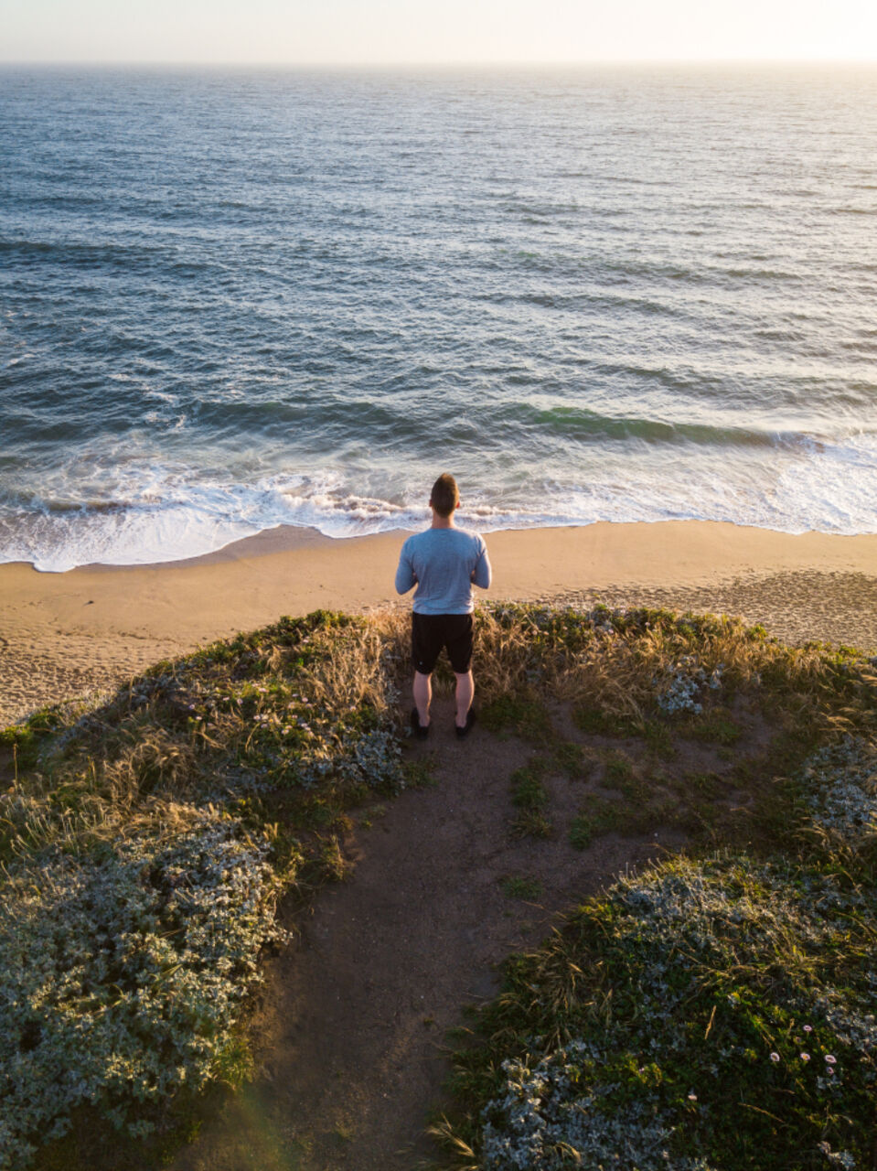 A man stands at the end of a path looking out at the sea.