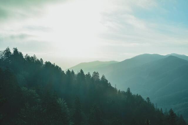 Photograph of clouds, forest, hills.