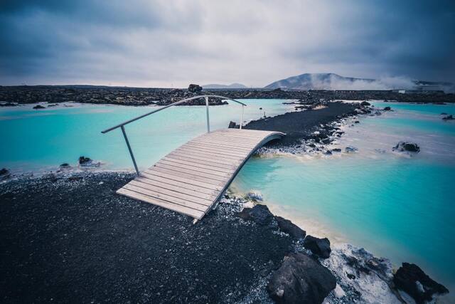 Photograph of beach, bridge, clouds.