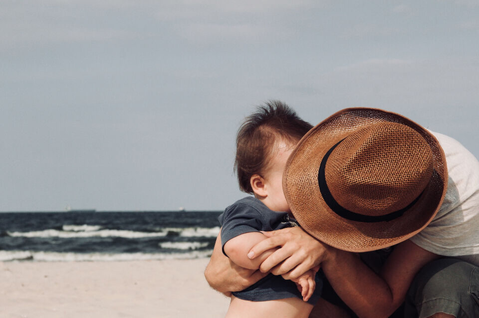 A father holds his young son by the sea.
