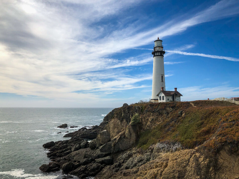 A white lighthouse on a rocky headland under a bright sky.