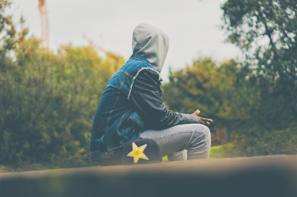 A man in a hooded jacket sits outdoors, looking away.
