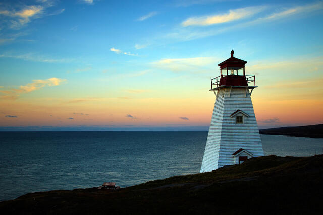 A white lighthouse above the sea at dusk.