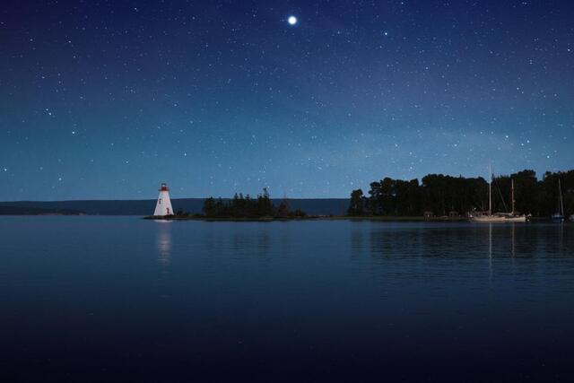 A small lighthouse shines across calm water at night.