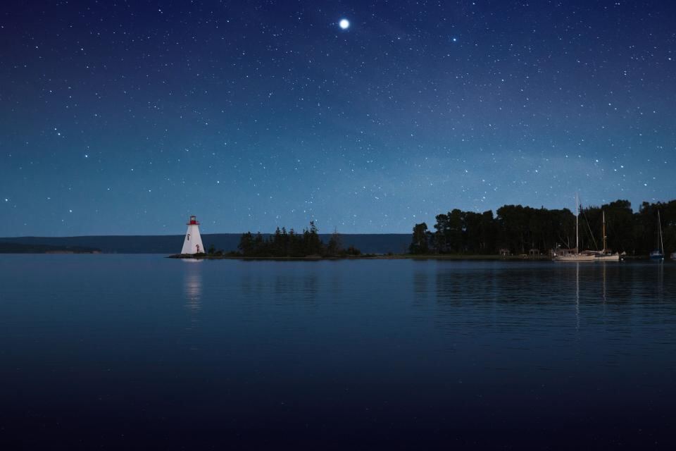 A small lighthouse shines across calm water at night.